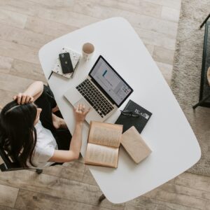 From above of young woman with long dark hair in casual clothes working at table and browsing netbook while sitting in modern workplace and touching hair